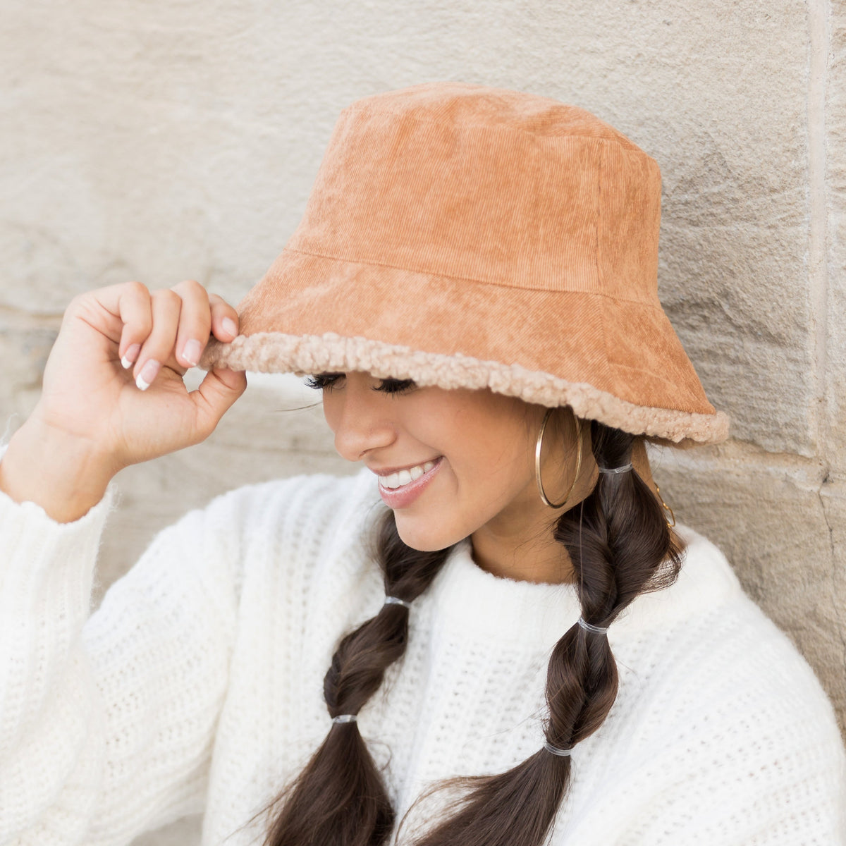Camel-colored reversible bucket hat worn with one hand at the brim.