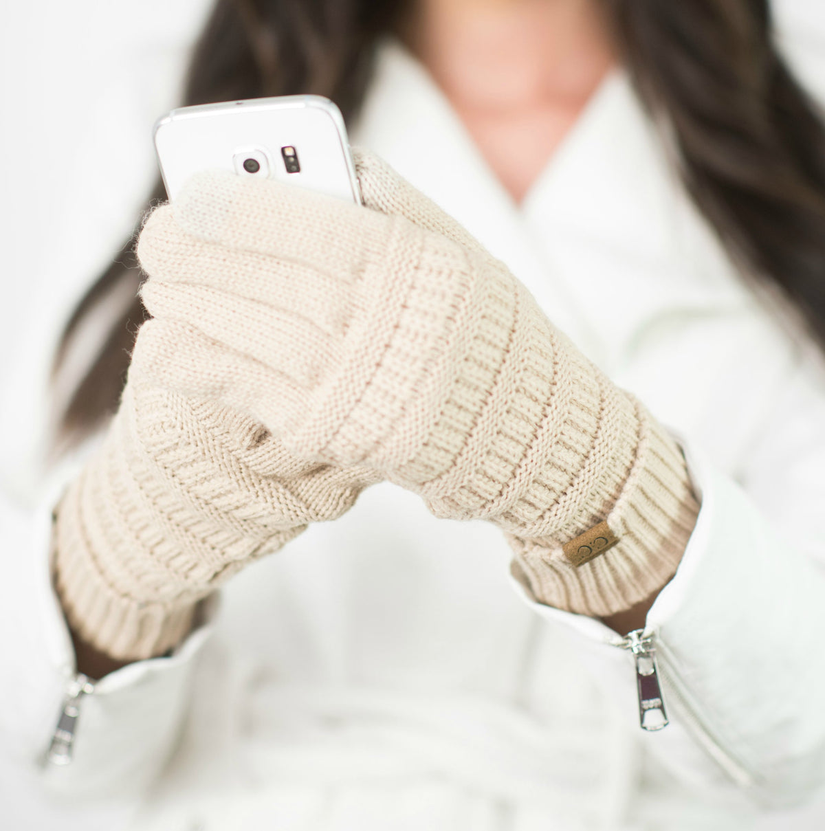 Beige cable-knit gloves shown with a white phone.