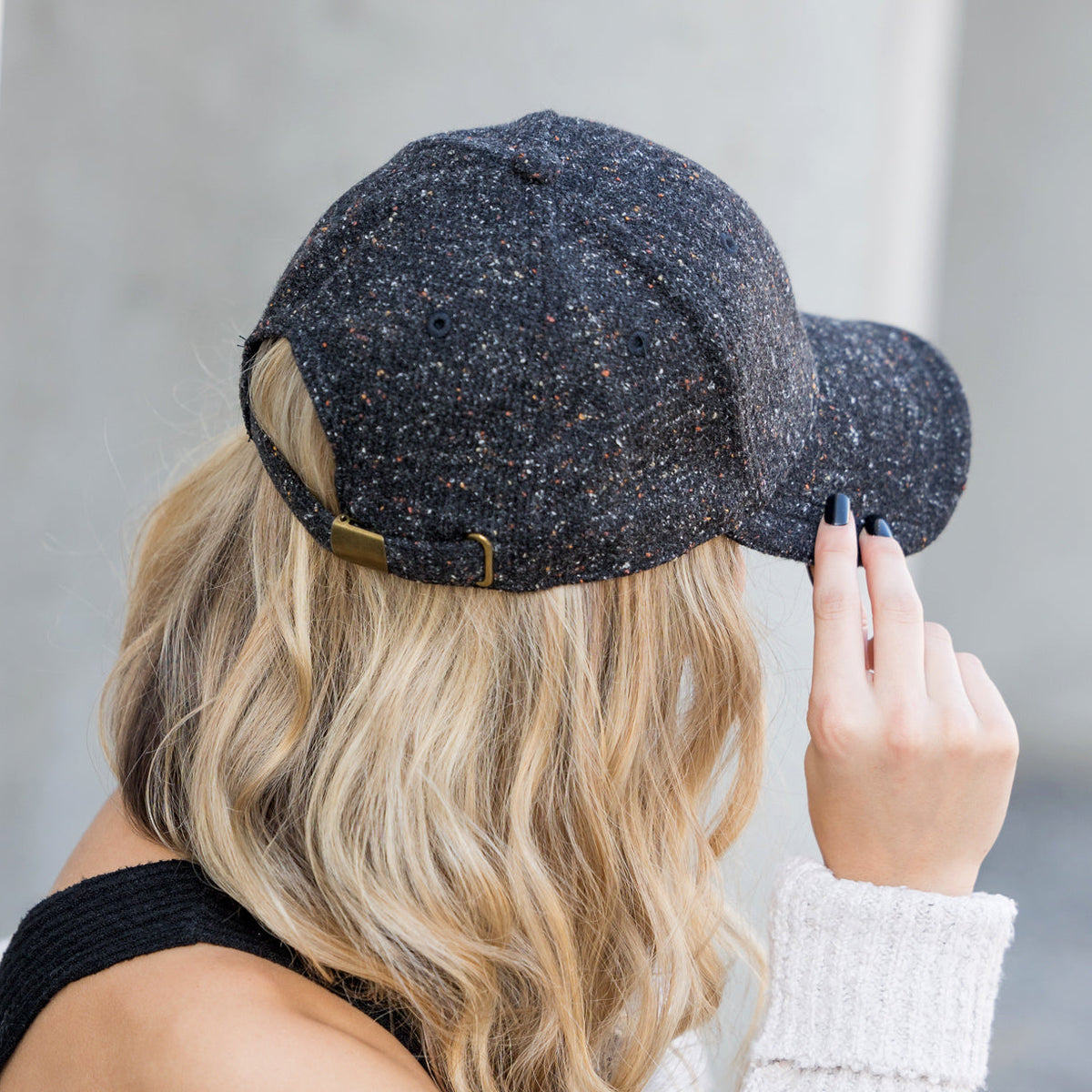 Rear view of a dark tweed-style baseball cap showing its adjustable clasp.