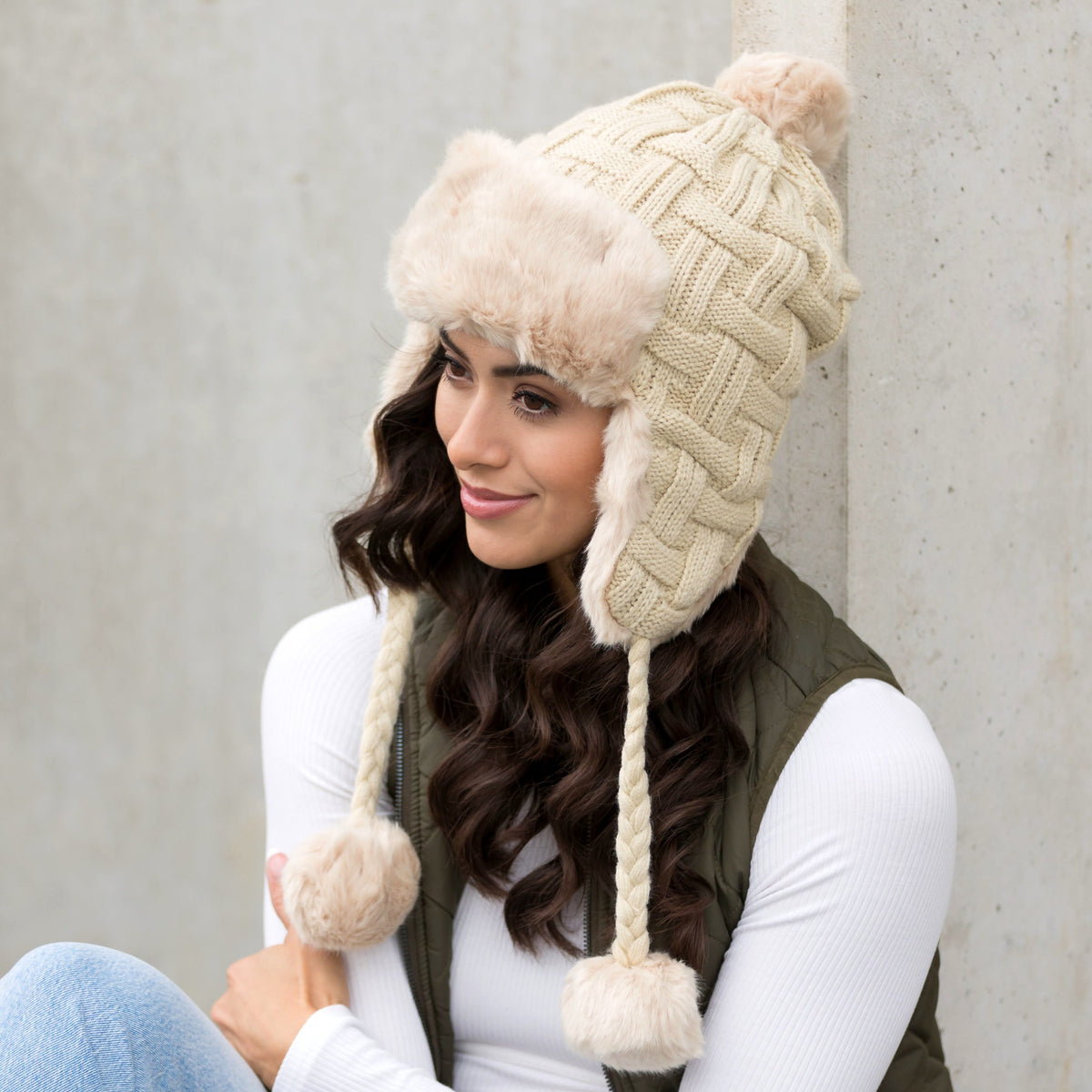 Beige cable-knit pom trapper hat shown from the side.