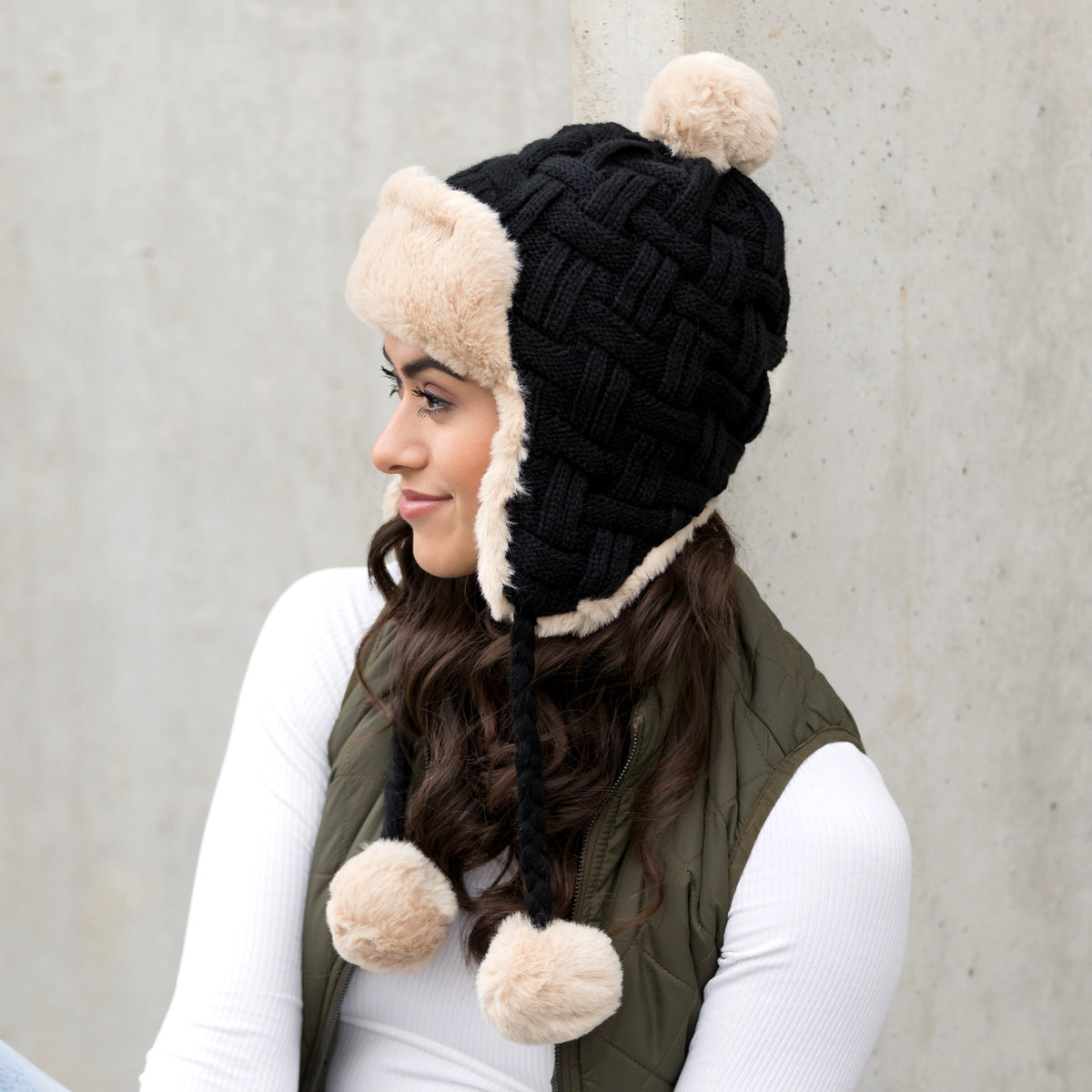 Black cable-knit pom trapper hat shown from the side.