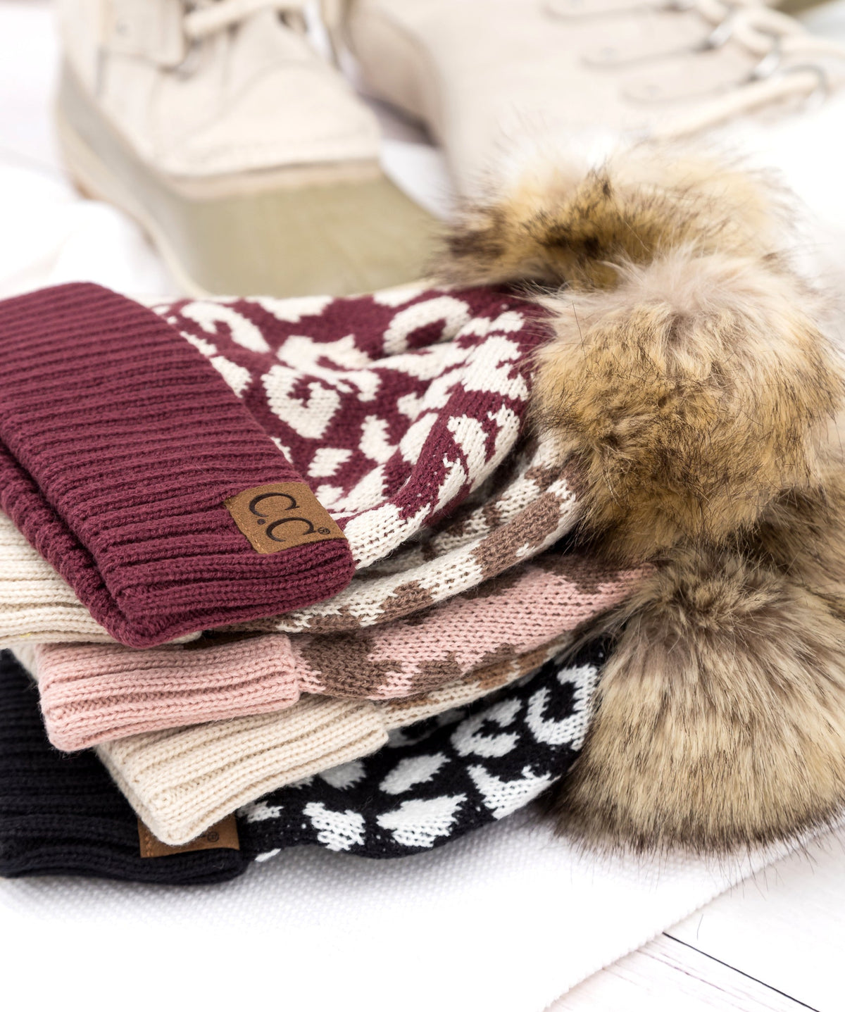 Stack of leopard-pattern pom beanies in several colors.