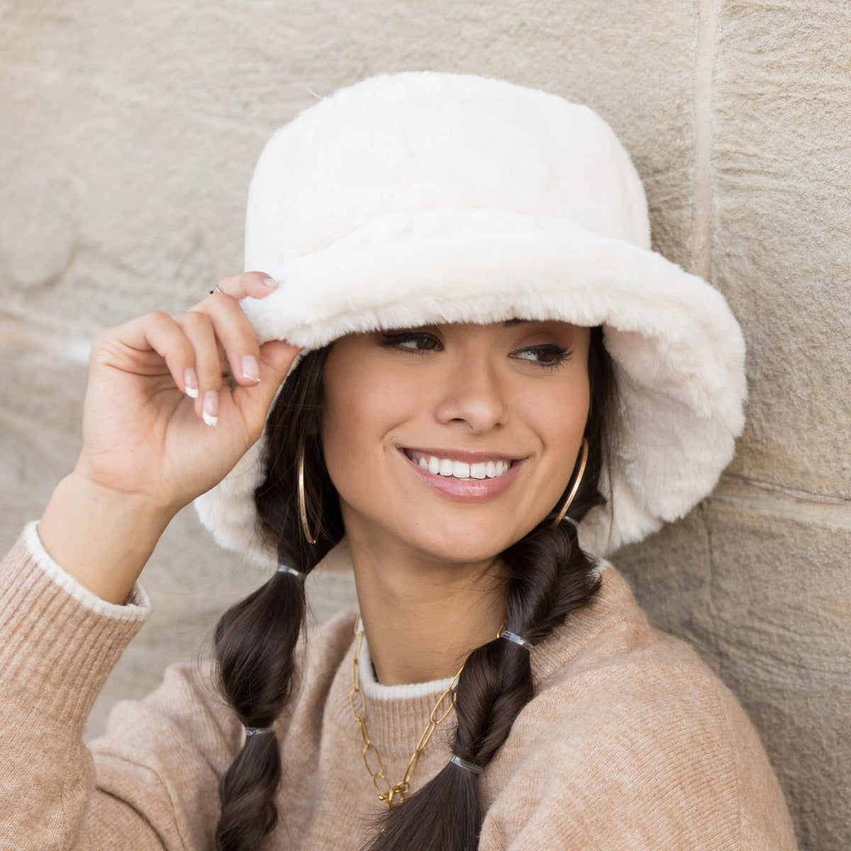 Cream plush bucket hat worn with both hands at the brim.