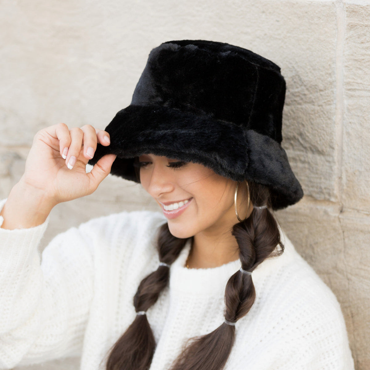 Black plush bucket hat worn with one hand at the brim.