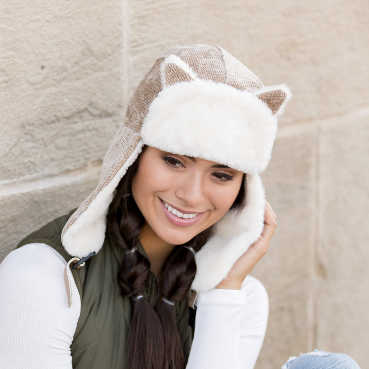 Taupe kitten-ear trapper hat with white trim and long ear flaps worn on a model.