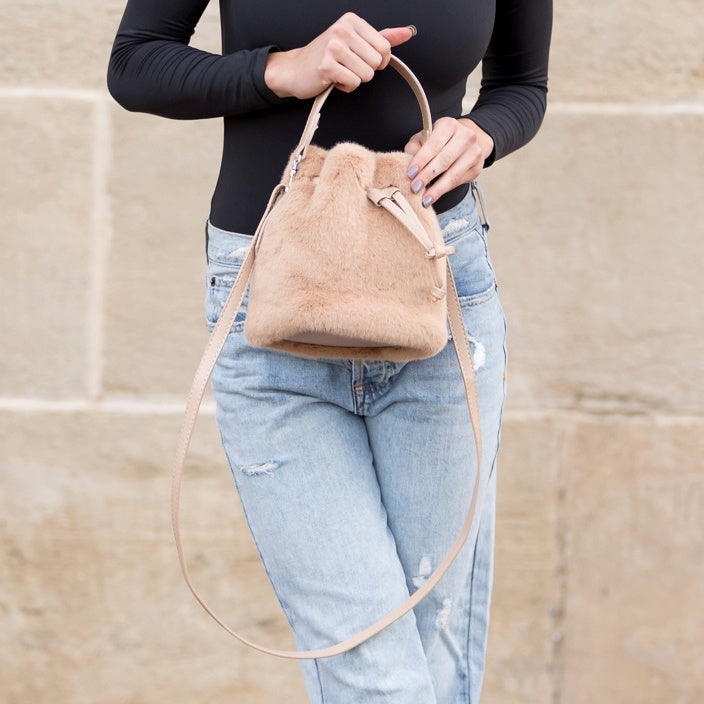 Camel plush drawstring bag held by its top handle.