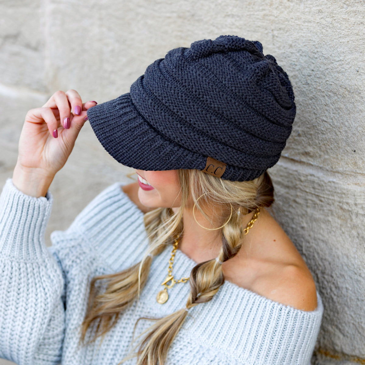 Dark knit brimmed cap worn with one hand at the brim.