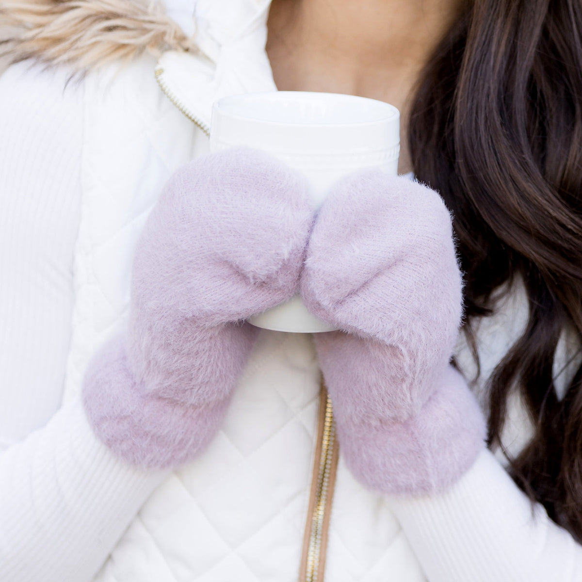Lavender plush mittens worn together in front of a light top.