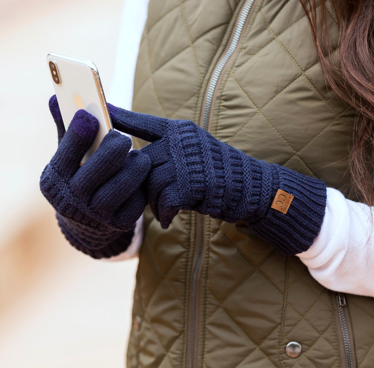 Navy cable-knit gloves worn while holding a phone.