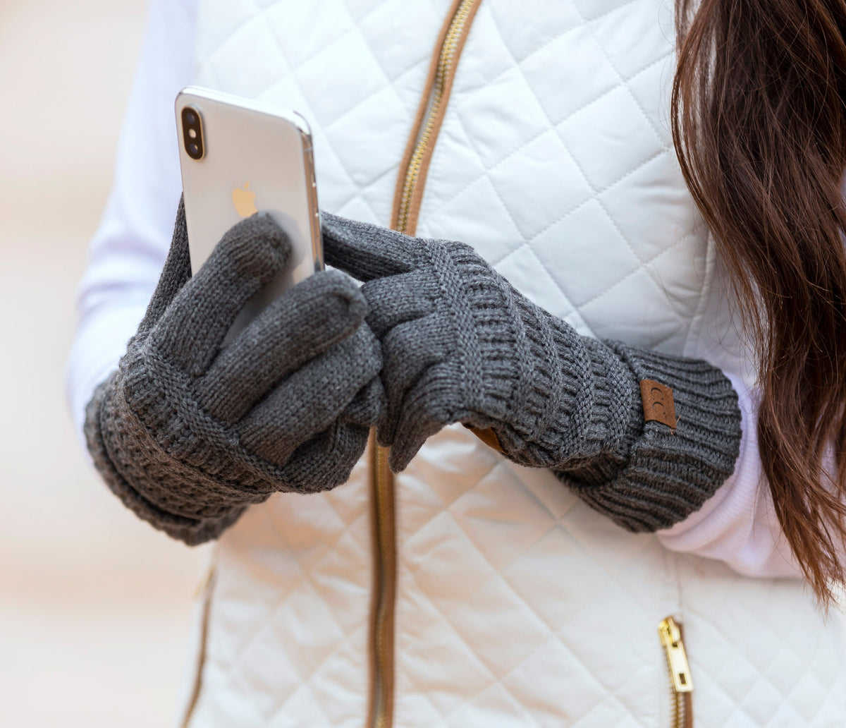 Dark grey cable-knit gloves worn while holding a phone.