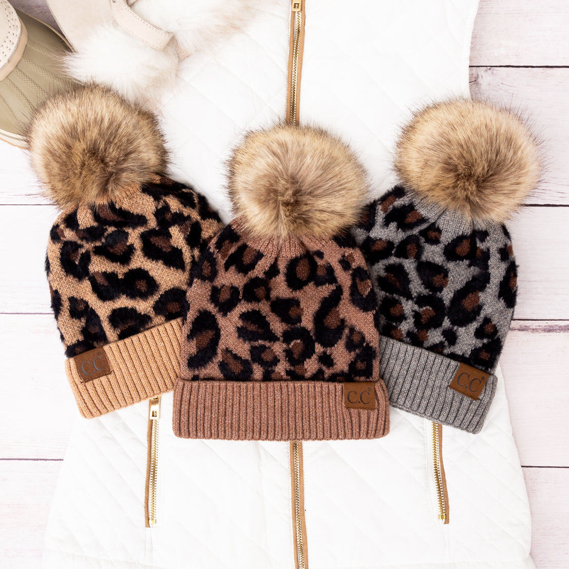 Three leopard-print pom beanies in brown and grey shades arranged together.