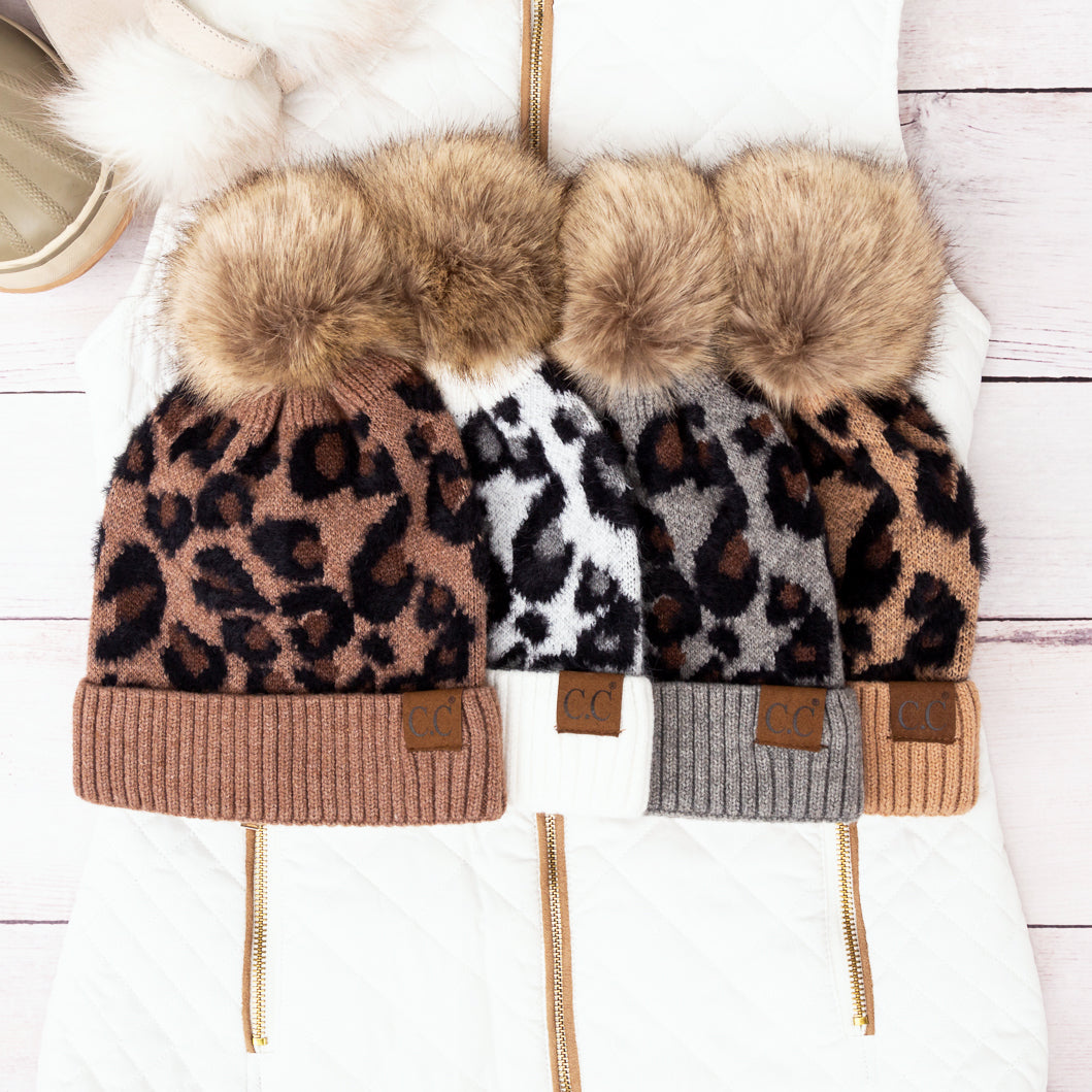Four leopard-print pom beanies arranged together.