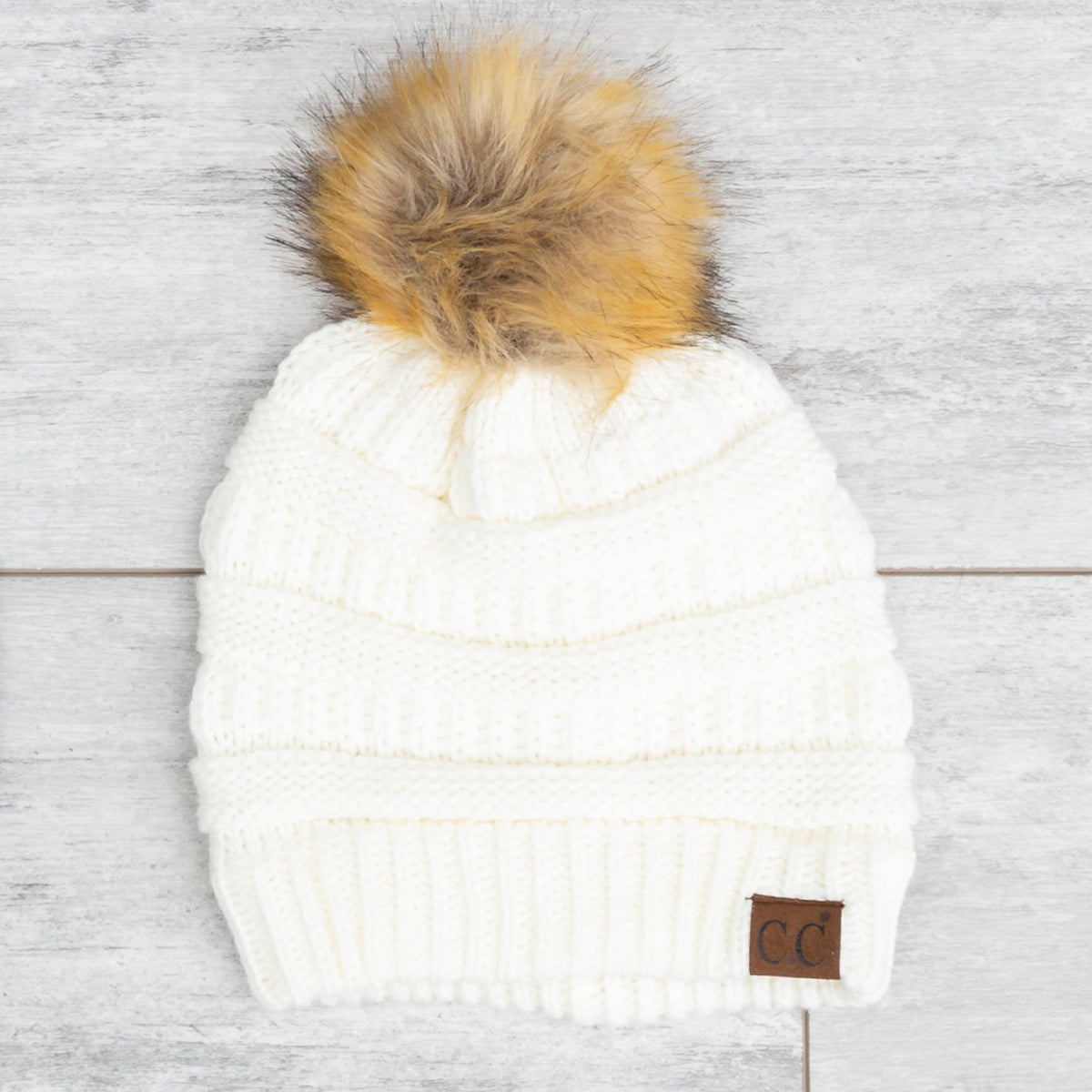White textured knit pom beanie on a pale wooden background.