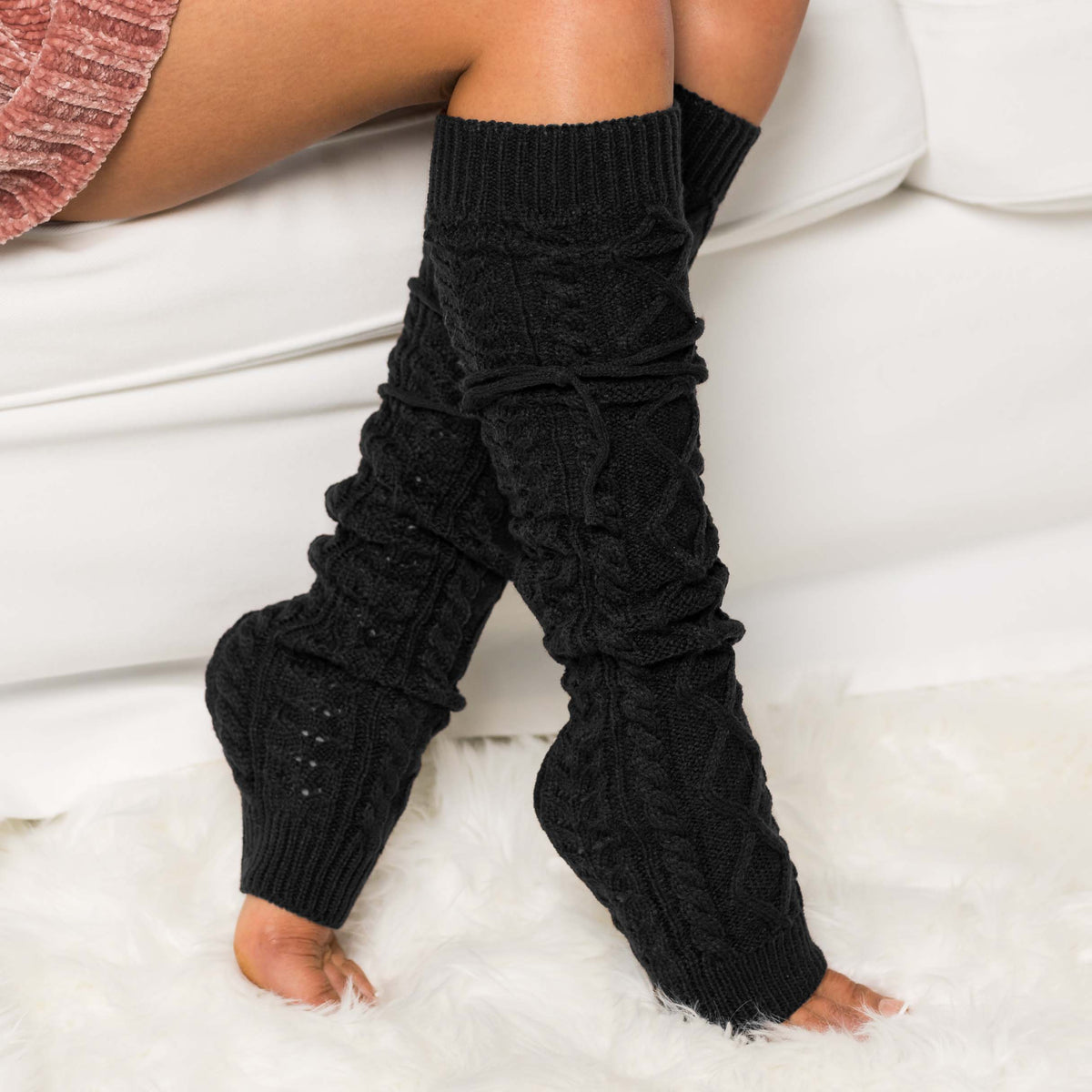 Black cable-knit leg warmers worn on a seated model.