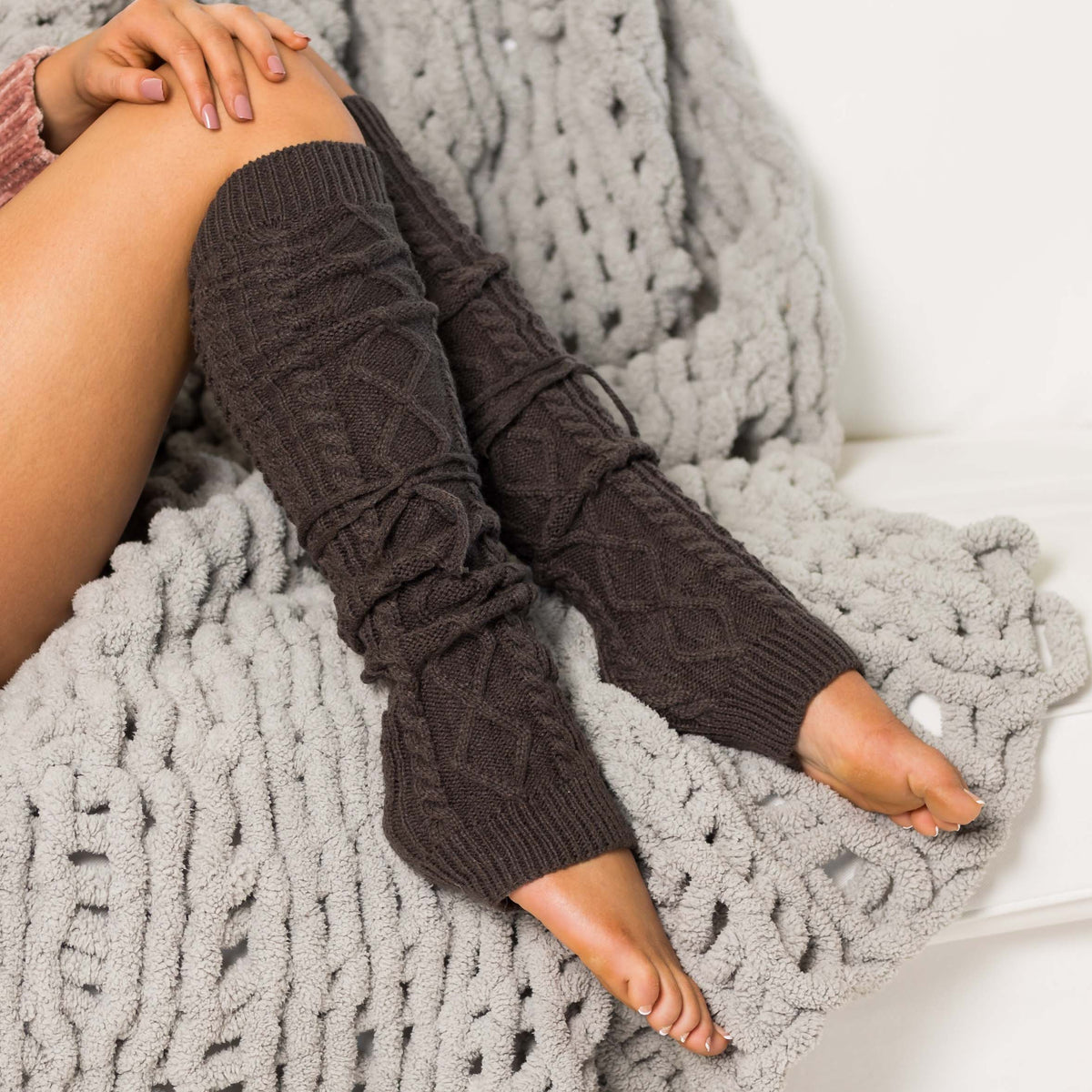 Charcoal cable-knit leg warmers worn with bare feet.