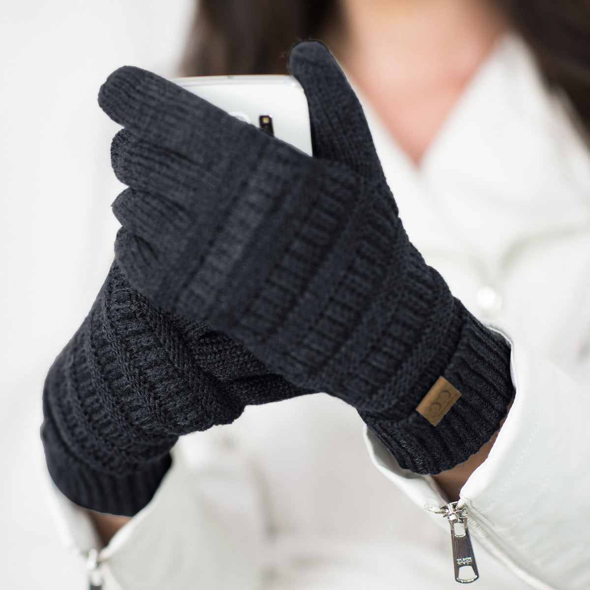 Black cable-knit gloves worn while holding a phone.