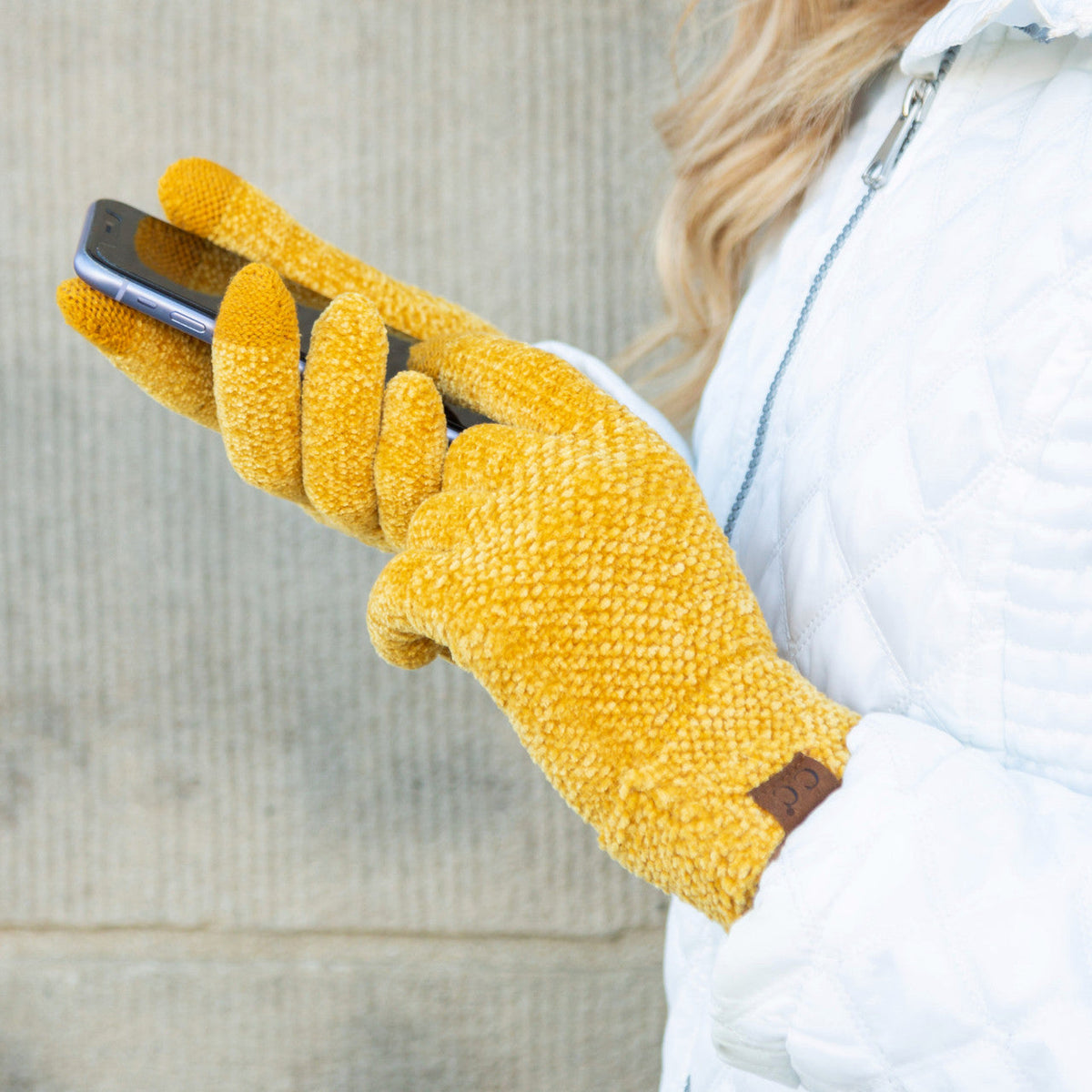 Mustard yellow textured gloves worn while holding a phone.