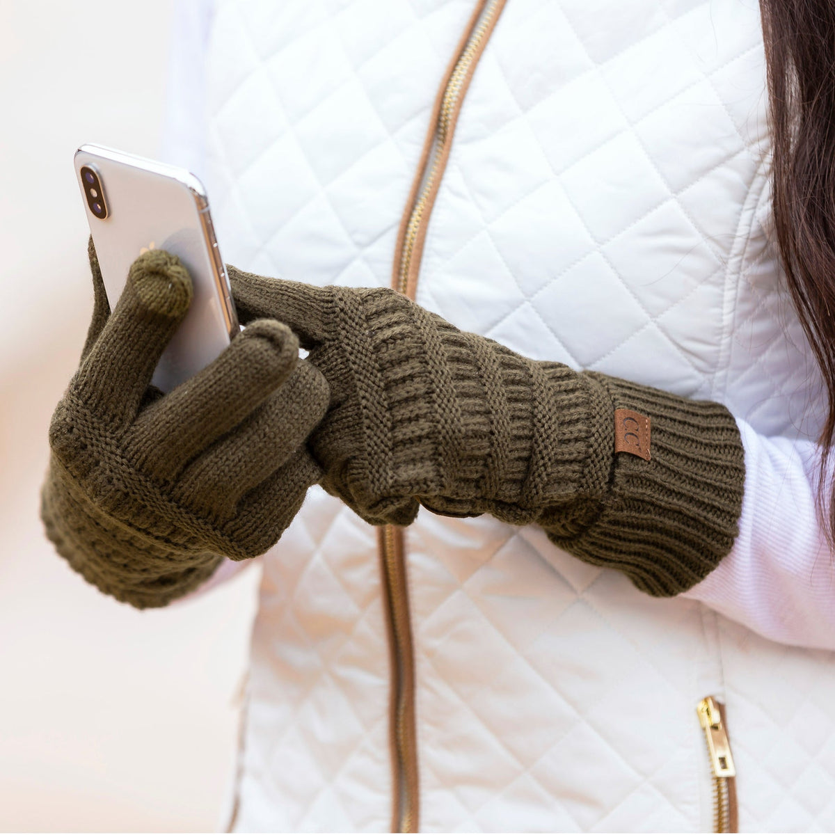 Olive green cable-knit gloves worn while holding a phone.