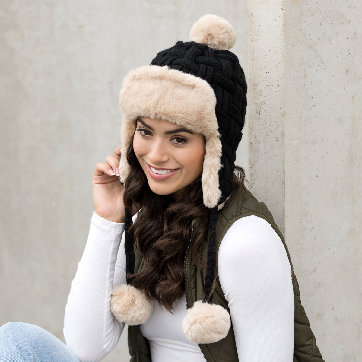 Black cable-knit trapper hat with light trim worn on a model.