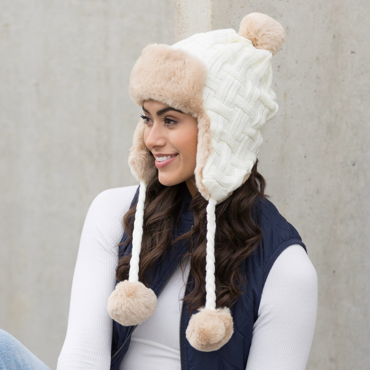 Ivory cable-knit pom trapper hat shown from the side.