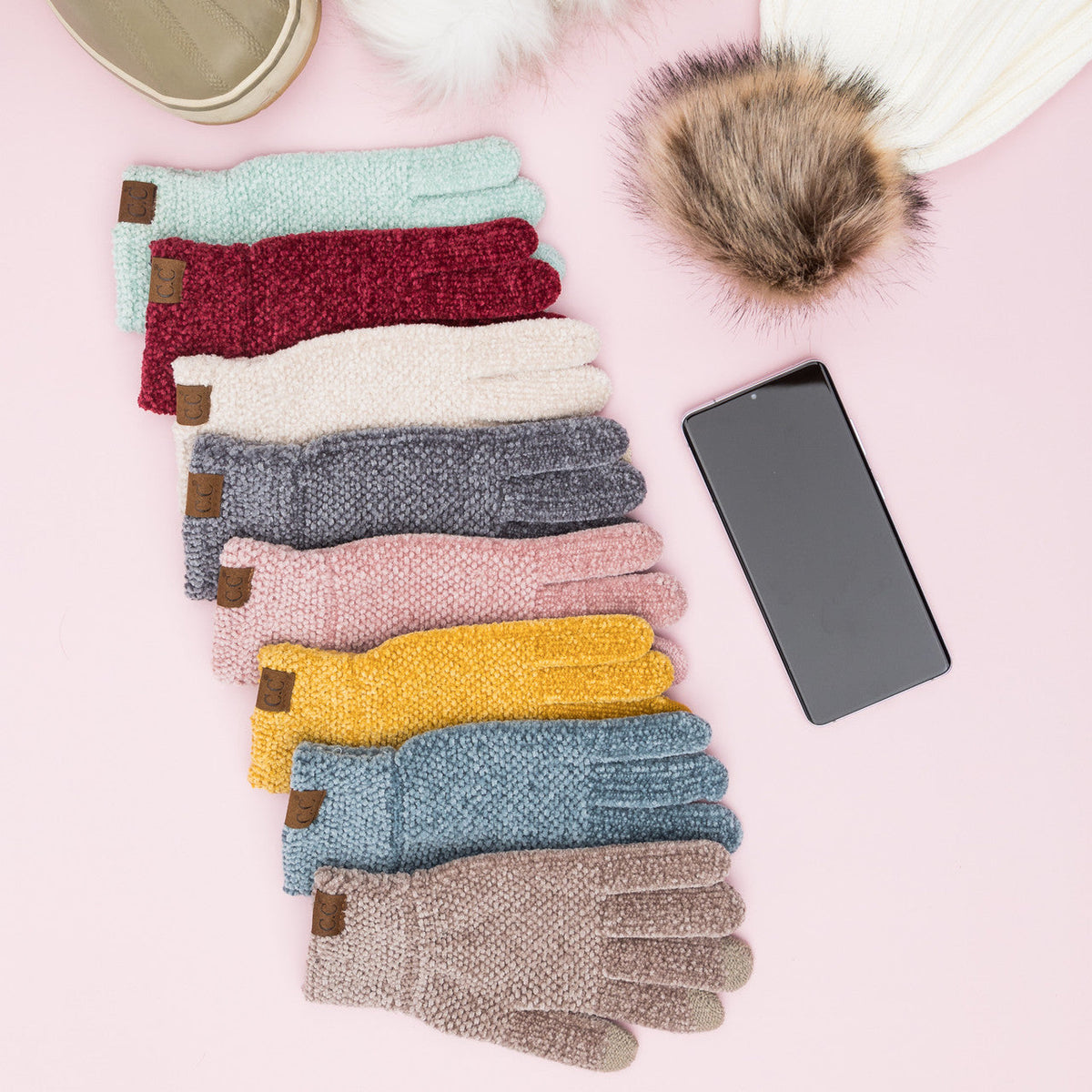 Assorted textured gloves laid out beside a phone and other styling props.