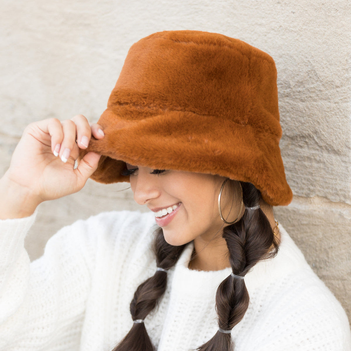Camel-colored plush bucket hat worn with one hand at the brim.