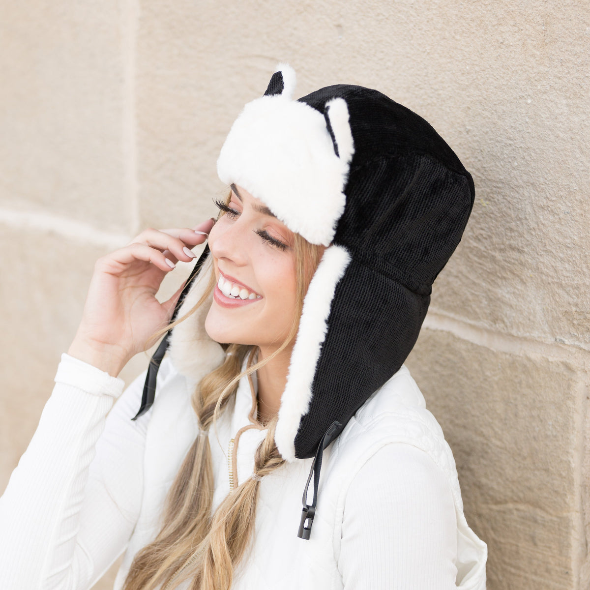 Black kitten-ear trapper hat with white trim worn on a model.