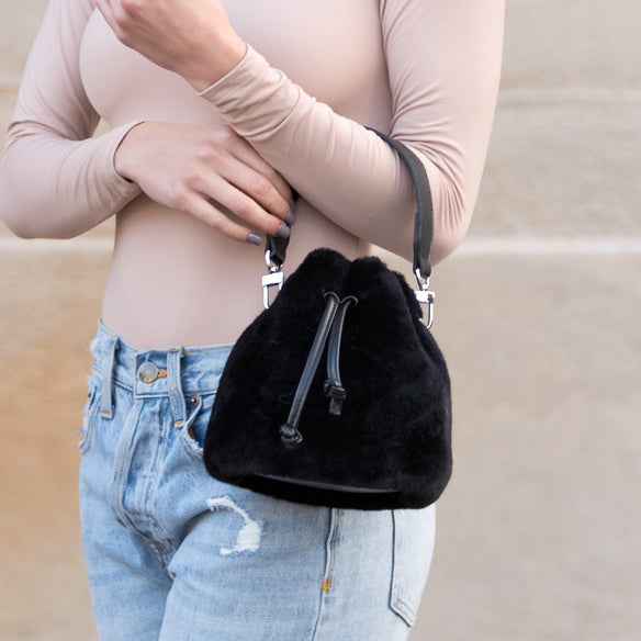 Black plush drawstring bag carried at the elbow.