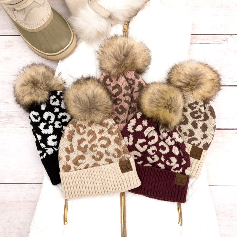Leopard-pattern pom beanies arranged in several colors.