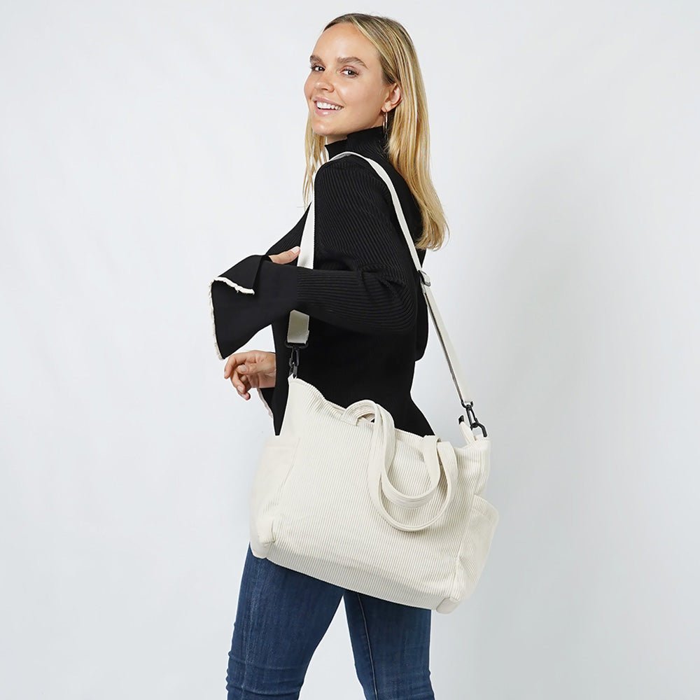 Woman holding ivory corduroy multi-pocket tote bag with crossbody strap