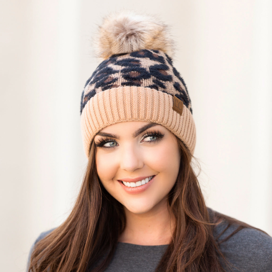 Tan and black leopard-print pom beanie worn on a model.