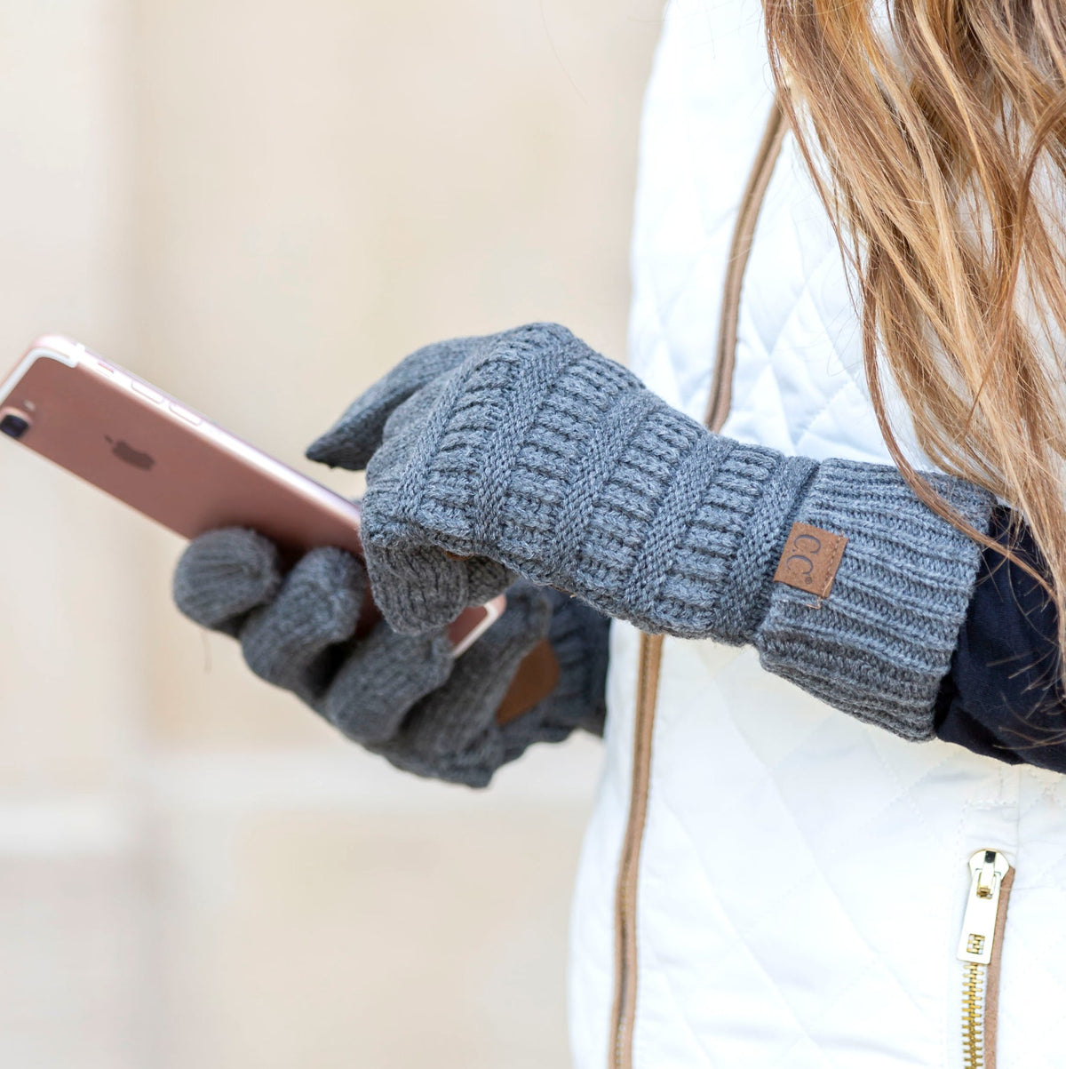 Blue-grey cable-knit gloves worn while holding a phone.