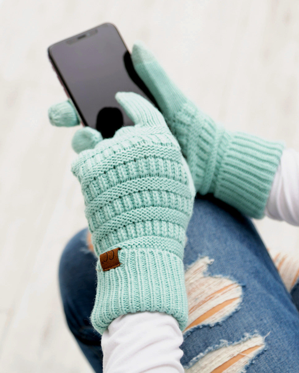 Mint cable-knit gloves worn while holding a phone.