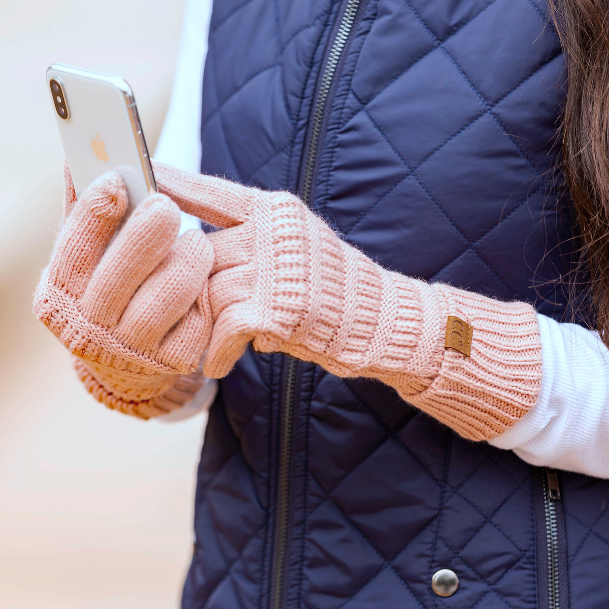 Pink cable-knit gloves shown from another angle with a phone.