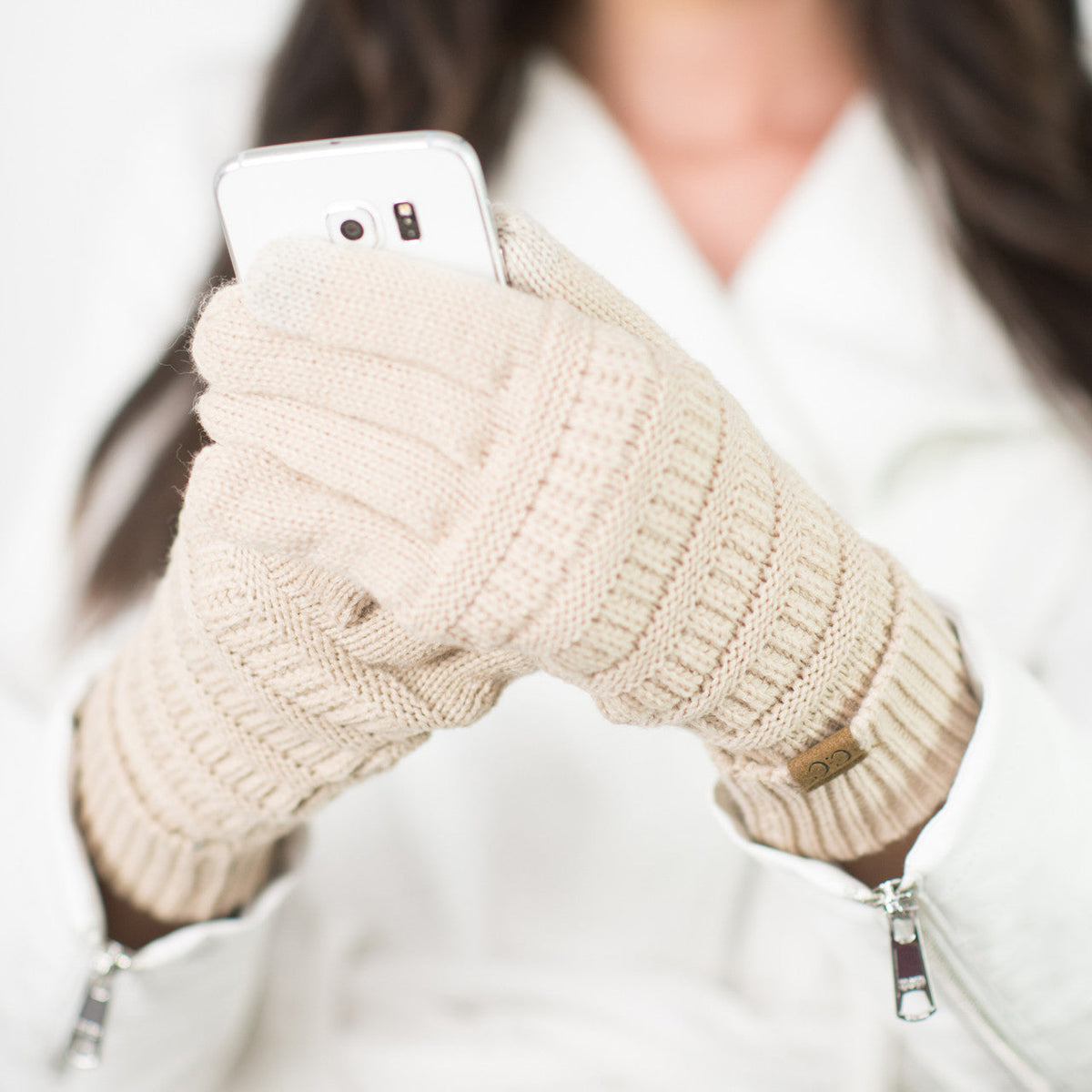Beige cable-knit gloves worn while holding a white phone.
