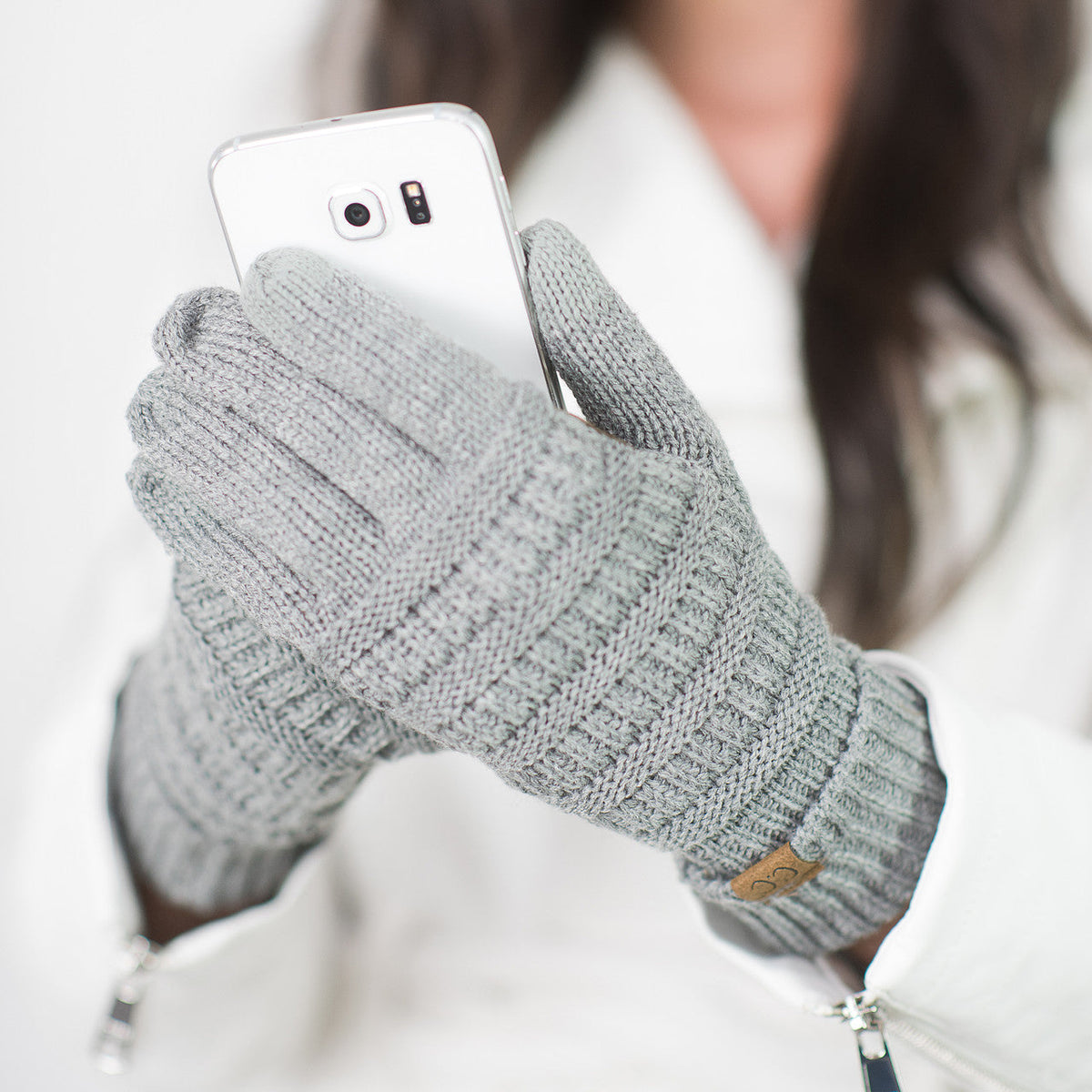 Light grey cable-knit gloves worn while holding a white phone.