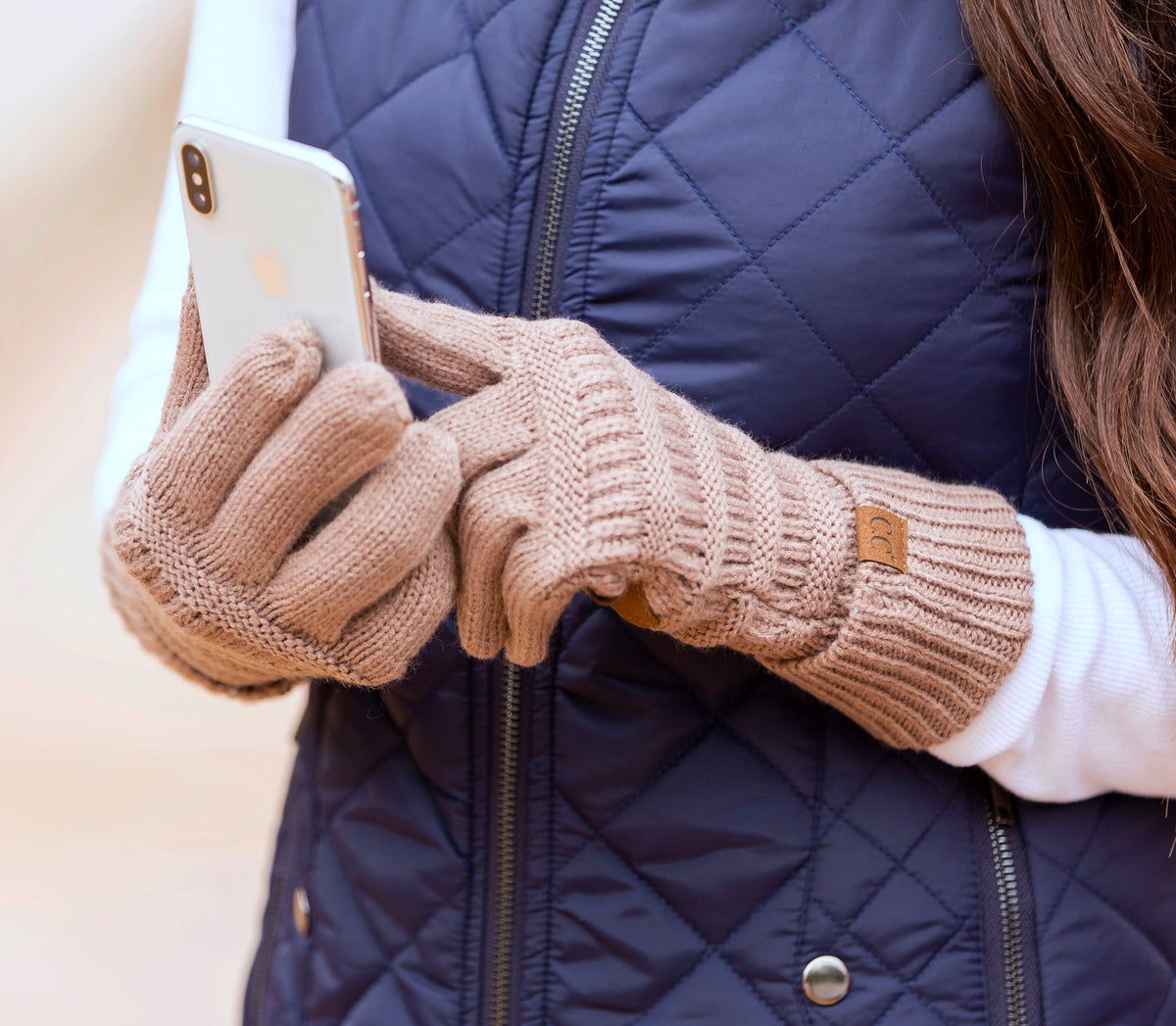 Pink cable-knit gloves worn while holding a phone.